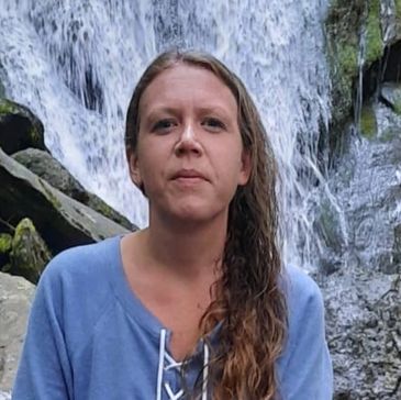 Woman standing in front of a waterfall wearing a blue sweatshirt.