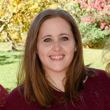 Young woman smiling outdoors with fall foliage.