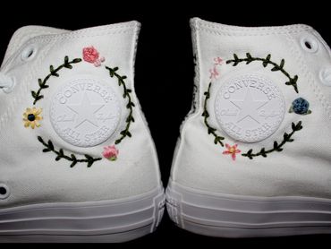 White Converse shoes with floral embroidery around the logo.