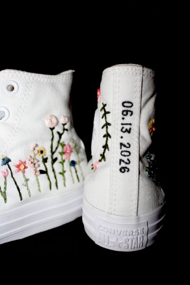White Converse shoes with floral embroidery and a date on the heel.