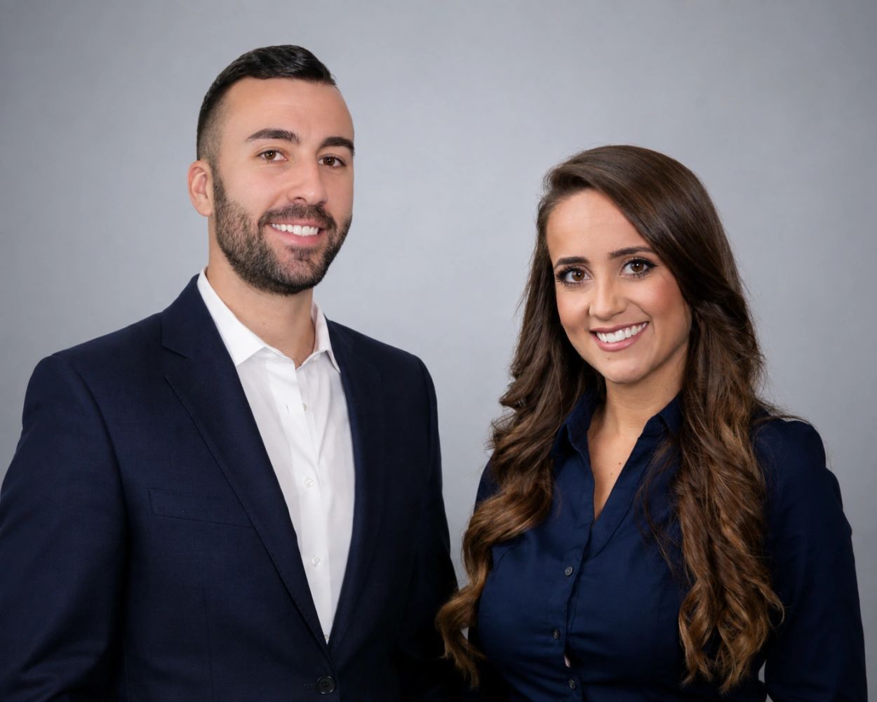 A man and woman in business attire smiling against a gray background.