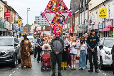 Man with colorful headgear leading a diverse group on a city street.