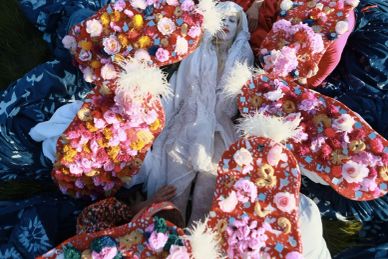 A person in white surrounded by colorful flower arrangements.