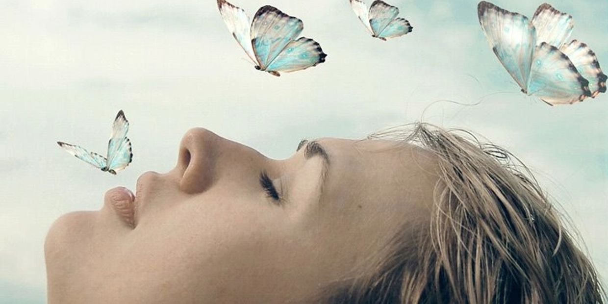 Woman lying down with closed eyes surrounded by blue butterflies.