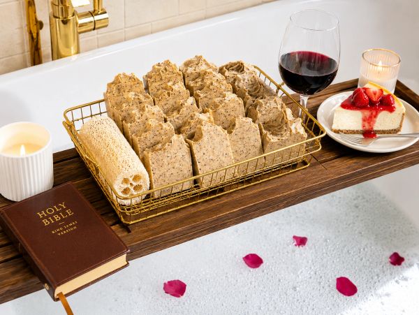 A relaxing bath setup with soap, wine, cheesecake, Bible, and candles on a wooden tray.