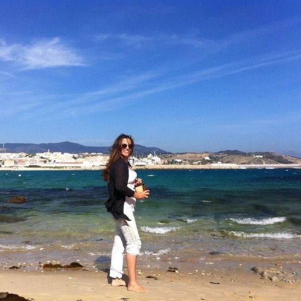 Woman enjoying a sunny day barefoot at a beach with a scenic ocean view.