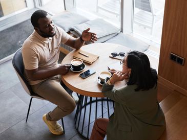 A male and female sat around a table with a coffee talking