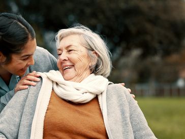 An elderly woman seated with a younger female behind her holding her shoulders
