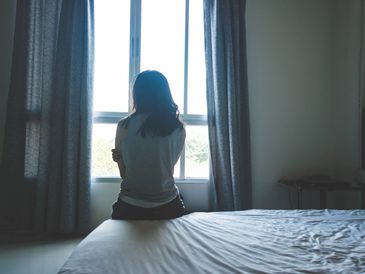 A woman sat on the edge of a bed looking out of a window