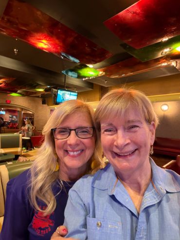 Two smiling women posing together indoors with colorful ceiling lights.