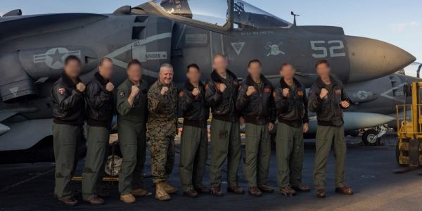 Group of military personnel posing in front of fighter jets.