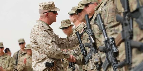 Military officer shaking hands with soldiers in uniform.