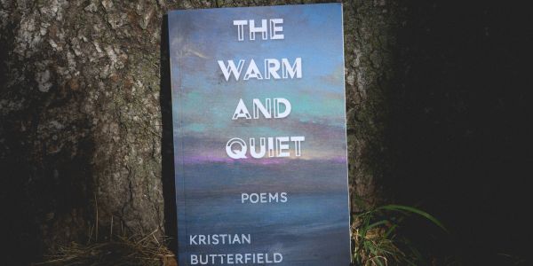 Poetry book titled The Warm and Quiet leaning against a tree.