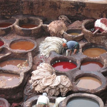 Workers processing animal hides in a traditional tannery with colorful dye pits.