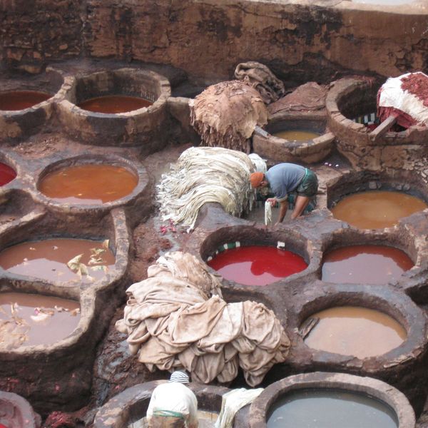 Workers processing animal hides in a traditional tannery with colorful dye pits.