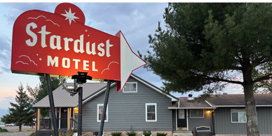 Red Stardust Motel sign with gray buildings and greenery in the background.