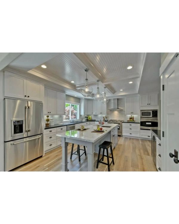 Modern white kitchen with stainless steel appliances and a central island with stools.
