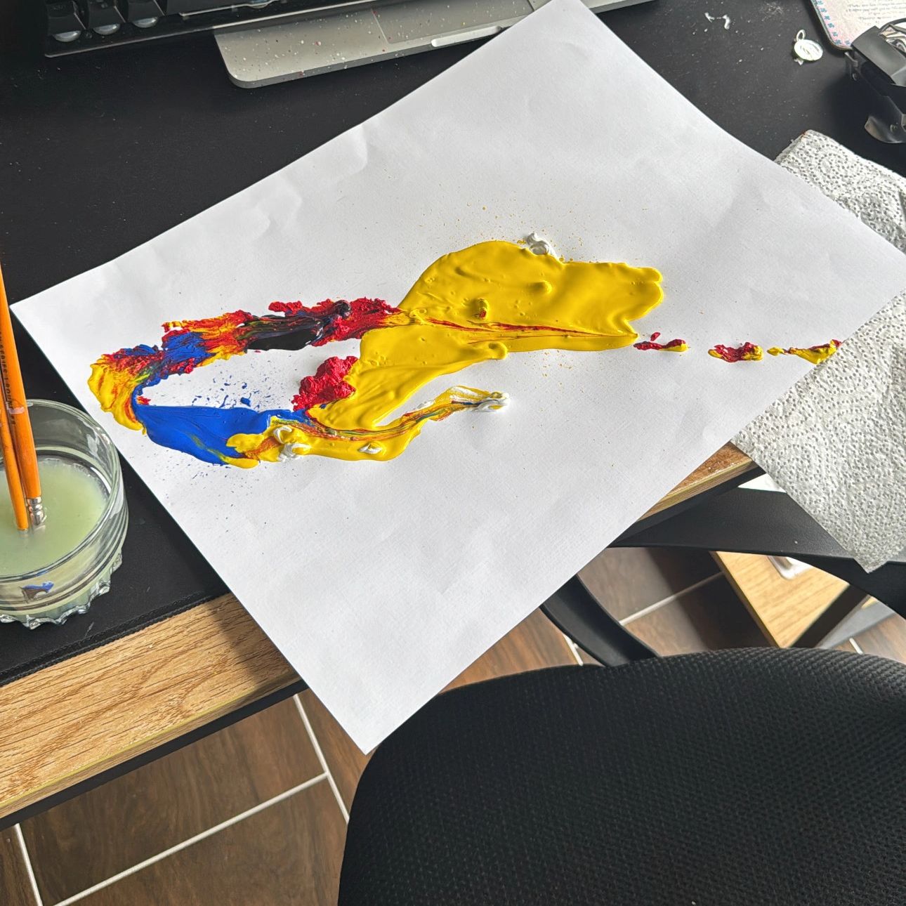 Palette of mixed bright paints on a white sheet next to brushes and water jar.