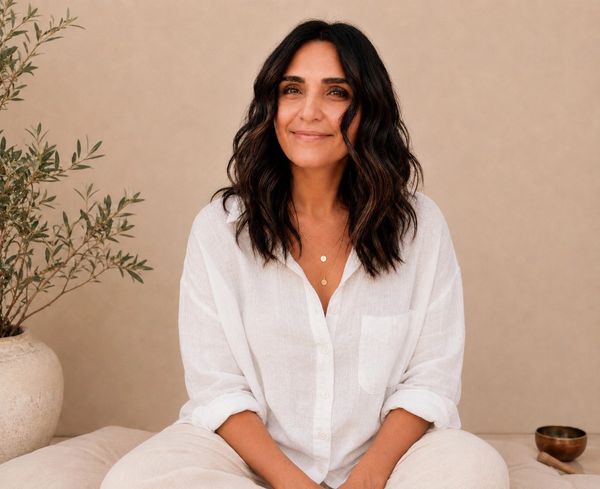 Woman smiling while sitting cross-legged against beige background.