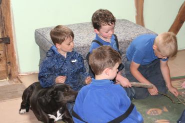 Four boys and a black dog sitting on the floor indoors.