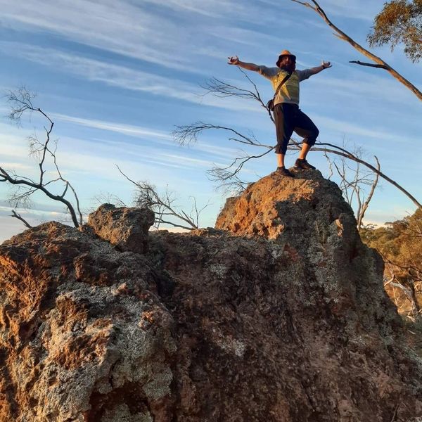 Person triumphantly stands on a rocky peak with arms spread wide under a clear sky.
