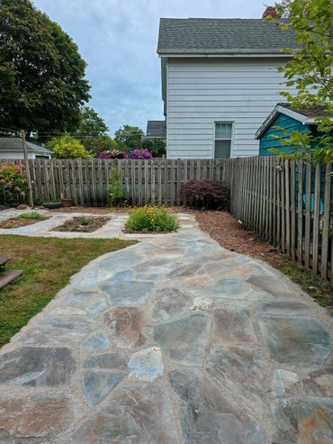 Stone pathway leading to a fenced backyard garden with flower beds.