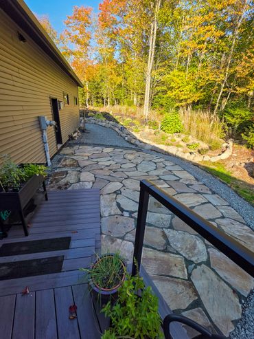 Stone pathway alongside a house with autumn trees in the background.