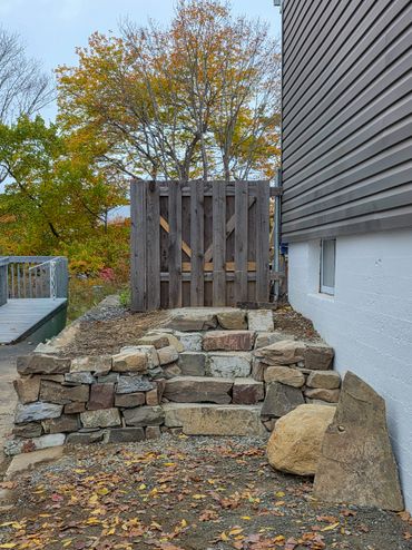 Stone steps leading to a wooden gate beside a house in autumn.