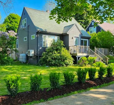Charming gray house with lush green lawn and vibrant shrubbery under clear blue sky.
