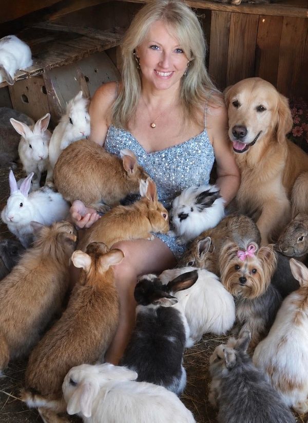 Smiling woman surrounded by many rabbits and a golden retriever dog.