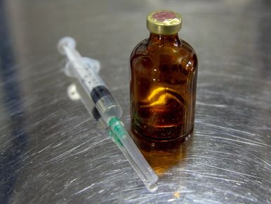 Syringe and amber vial on top of a metal exam table.