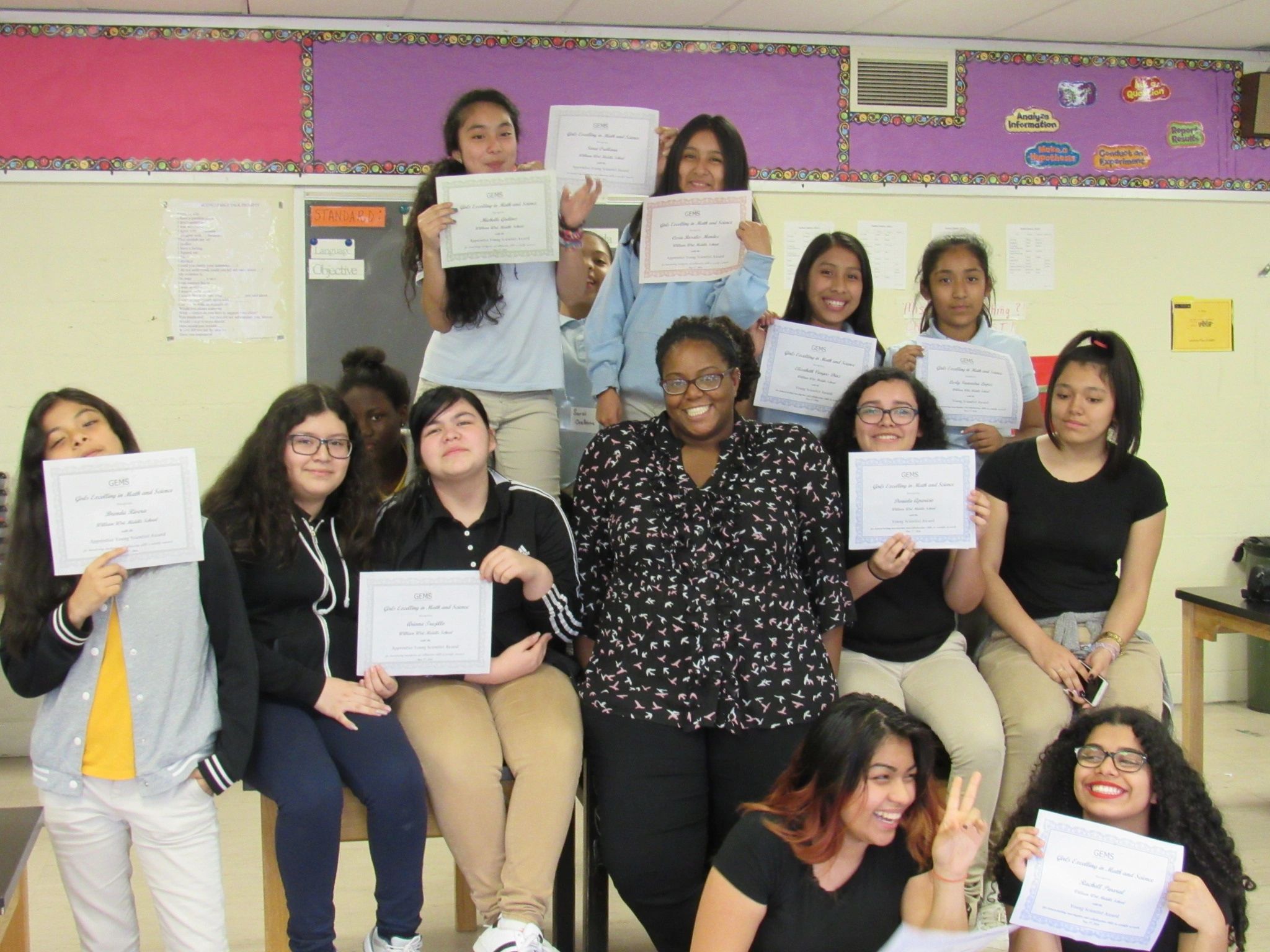 Students proudly display achievement certificates in a classroom setting.