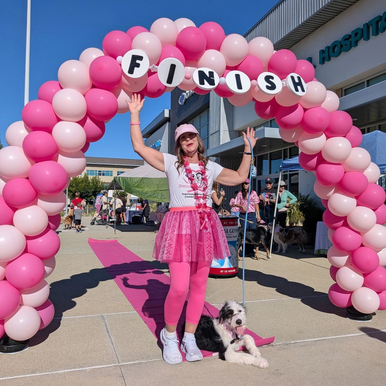 Woman and dog celebrating at a pink-themed finish line event.