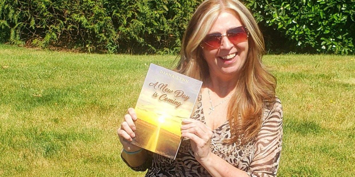 Woman smiling outdoors holding a book titled 'A New Day is Coming'.