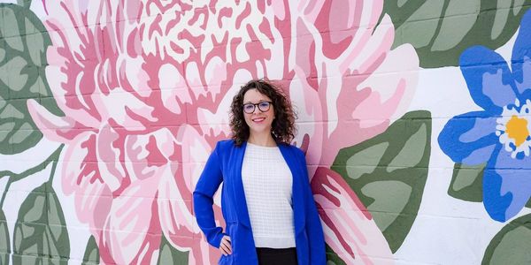 Photo of a smiling person in a blazer with a flower mural in the background