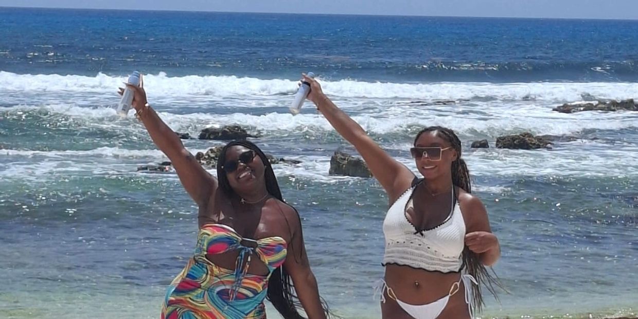 Two women in swimsuits cheer on a beach with ocean waves behind them.
