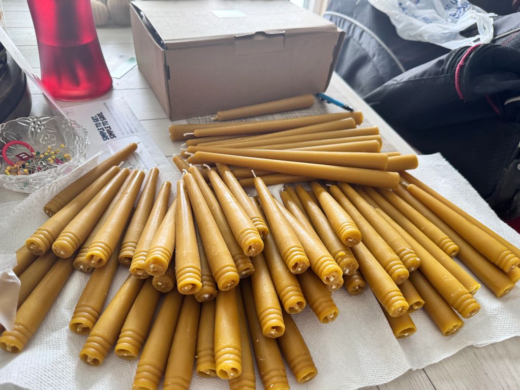 Handmade beeswax candles drying on a table with various supplies around.