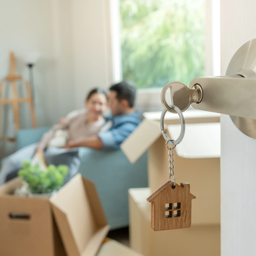 House key with a couple sitting on a couch amidst moving boxes.