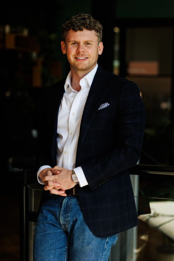 Man in a dark blazer and jeans smiling.