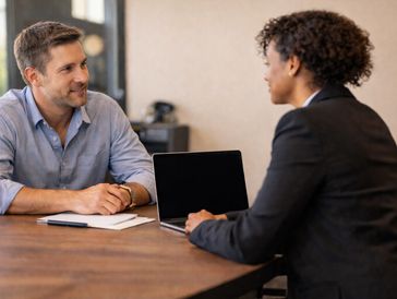 Two professionals engaged in a friendly meeting with a laptop and documents on the table.