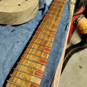 Unfinished guitar neck with metal frets and padauk inlays on a blue cloth.