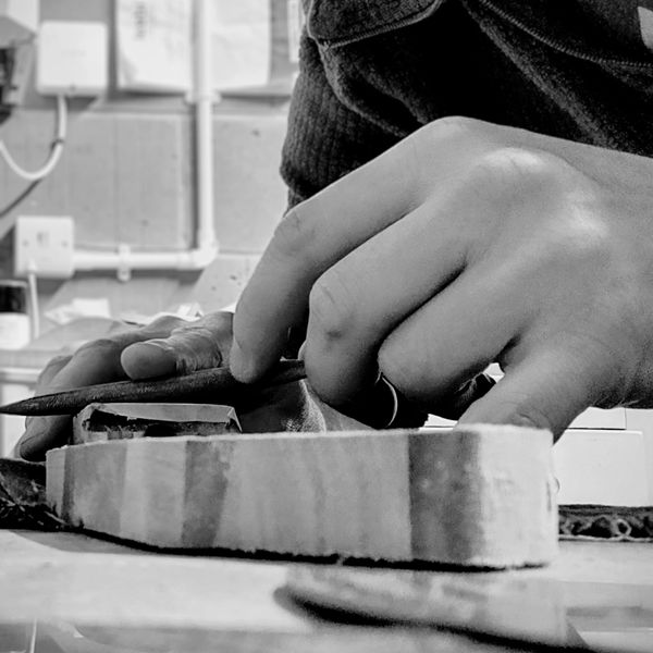 Close-up of hands carving a wooden piece with tools.