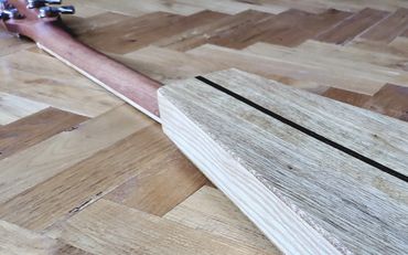 A wooden stringed musical instrument body on a parquet floor.