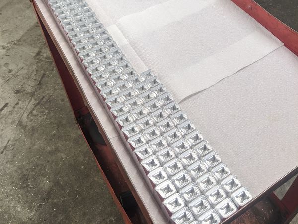 Rows of shiny metal square parts on a surface.