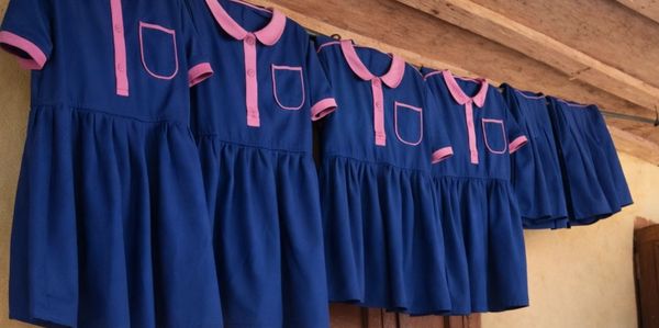 Blue and pink school uniforms hanging on a wooden beam.