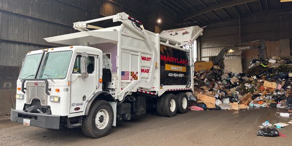 White garbage truck unloading waste inside a large facility.