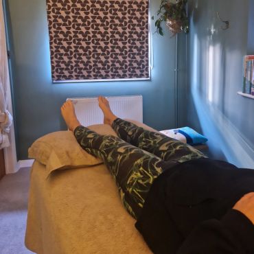 Person lying on a massage table in a cozy room with blue walls.