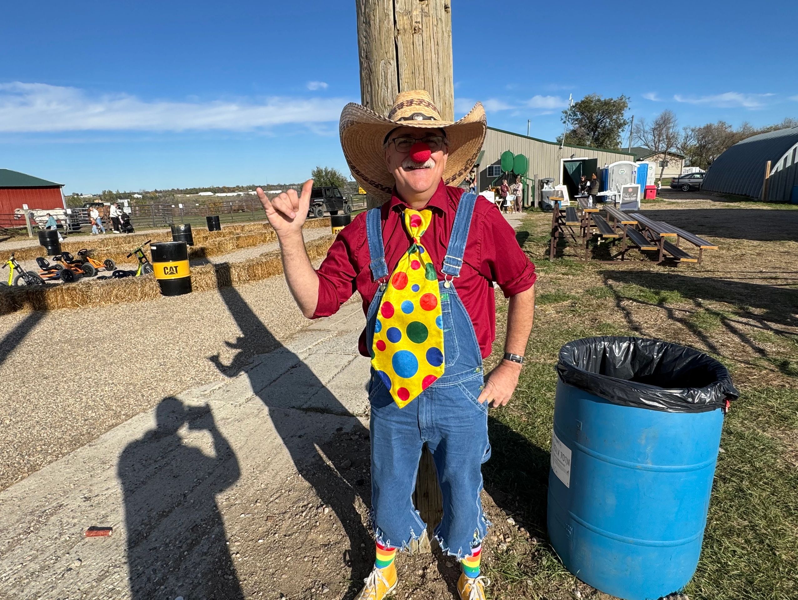Man dressed as a clown in overalls and a cowboy hat.