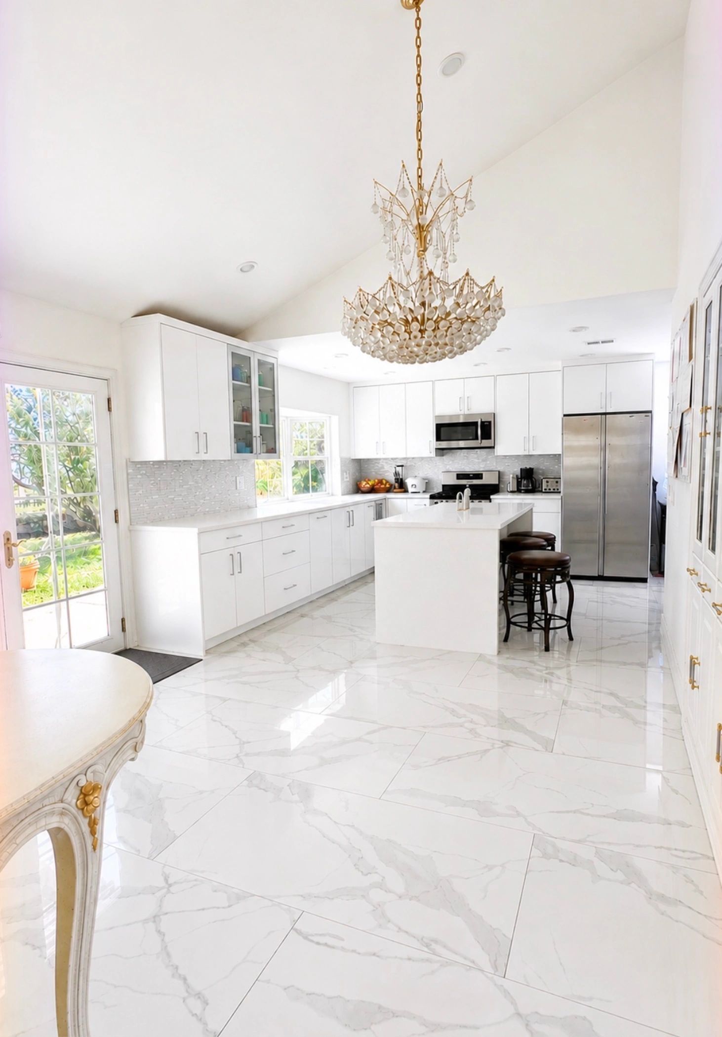 Bright white kitchen with marble floors and chandelier.