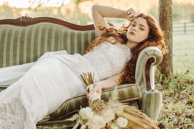 Red headed model laying on a green striped velvet couch with a boho inspired bouquet. 